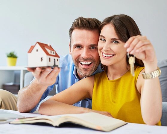 Happy Couple Holding Keys to New Home and House Miniature